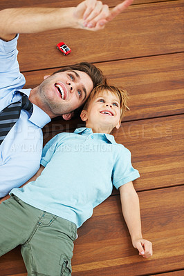 Buy stock photo A cute boy and his young father lying on the floor and looking up at something