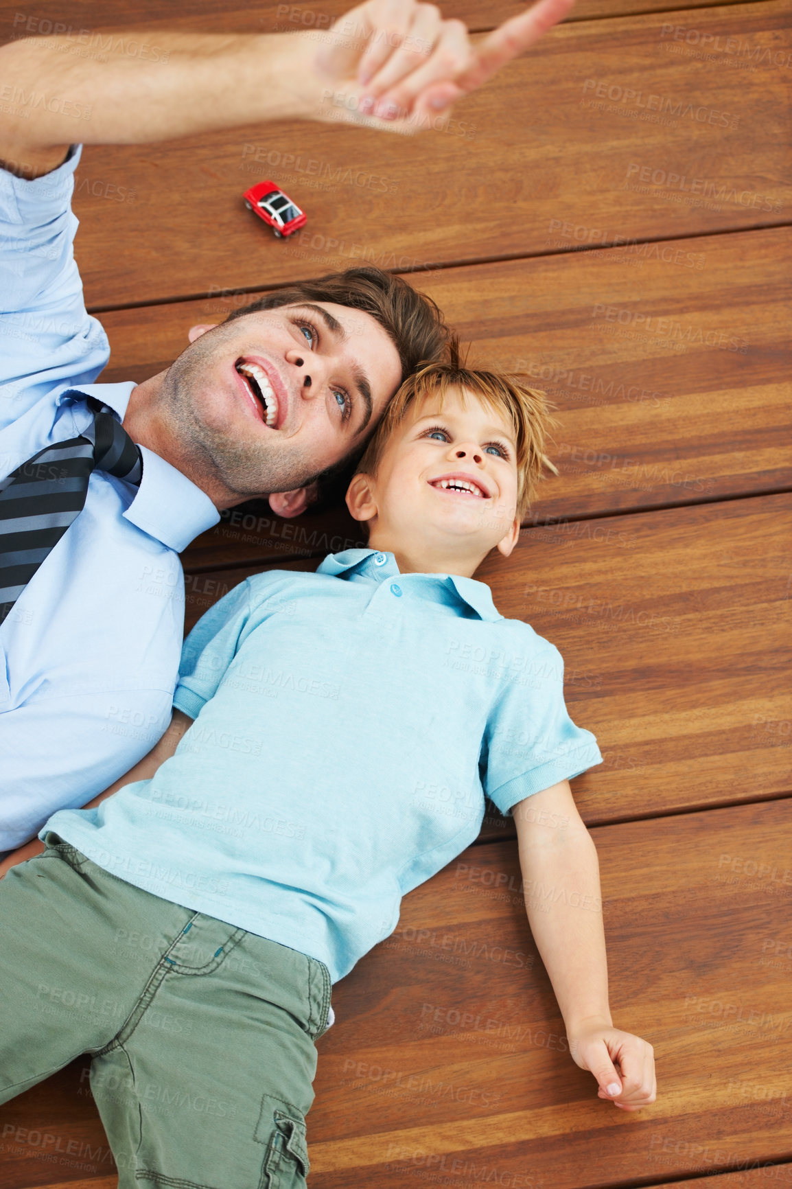 Buy stock photo A cute boy and his young father lying on the floor and looking up at something