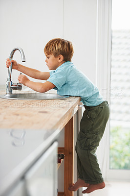 Buy stock photo A cute young boy climbing the kitchen counter to get to the tap