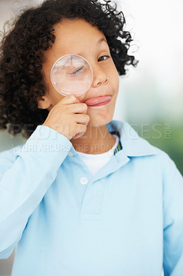 Buy stock photo Portrait of a cute young boy looking while holding a magnifying glass over his closed eye