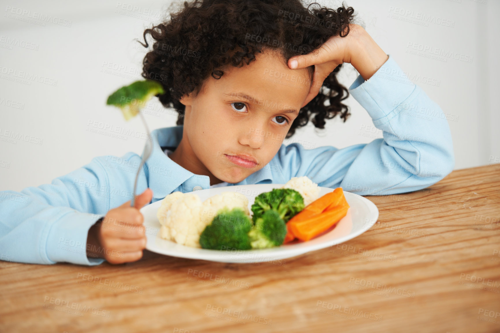 Buy stock photo Shot of an unimpressed-looking little boy sitting in front of a plate of vegetables
