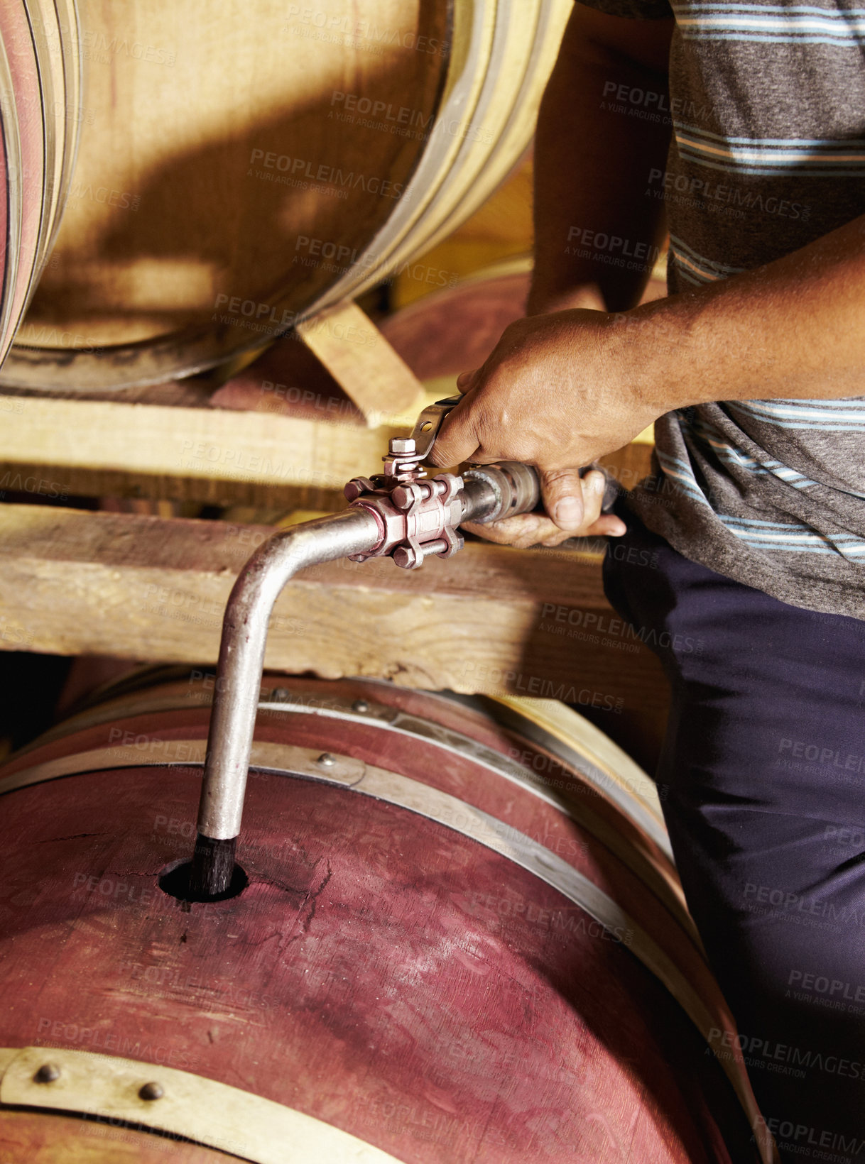 Buy stock photo A man racking a barrel in preparation for bottling wine.  
Closeup of a red wine barrel being refilled with wine by a cellar worker. Winemaker using iron pipe to pour red wine into wooden oak containers