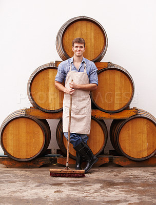 Buy stock photo Portrait, broom and oak barrels with a man cleaning the wine cellar of a beverage distillery. Confident, apron and a male cleaner in a winery for the production, fermentation or storage of alcohol