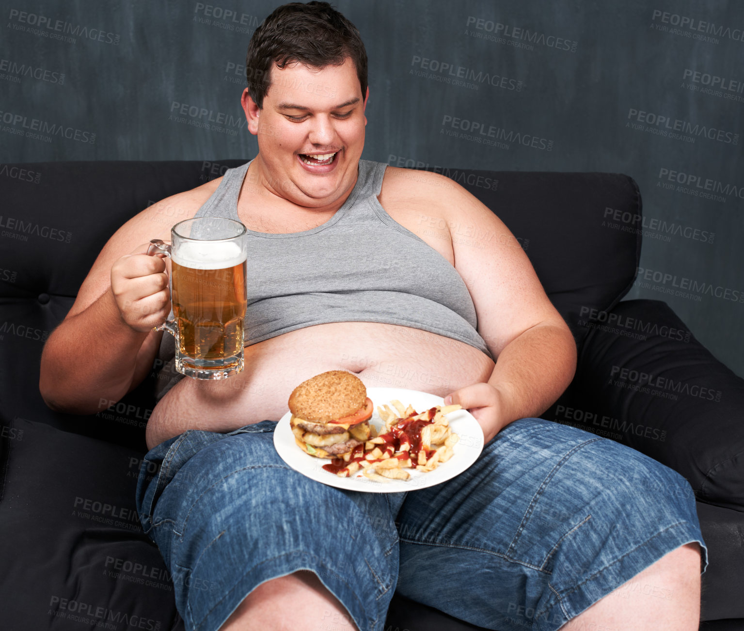 Buy stock photo An obese young man sitting on a sofa and gorging himself on beer and fast food