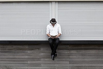 Buy stock photo A formally dressed man sitting on a ledge and reading