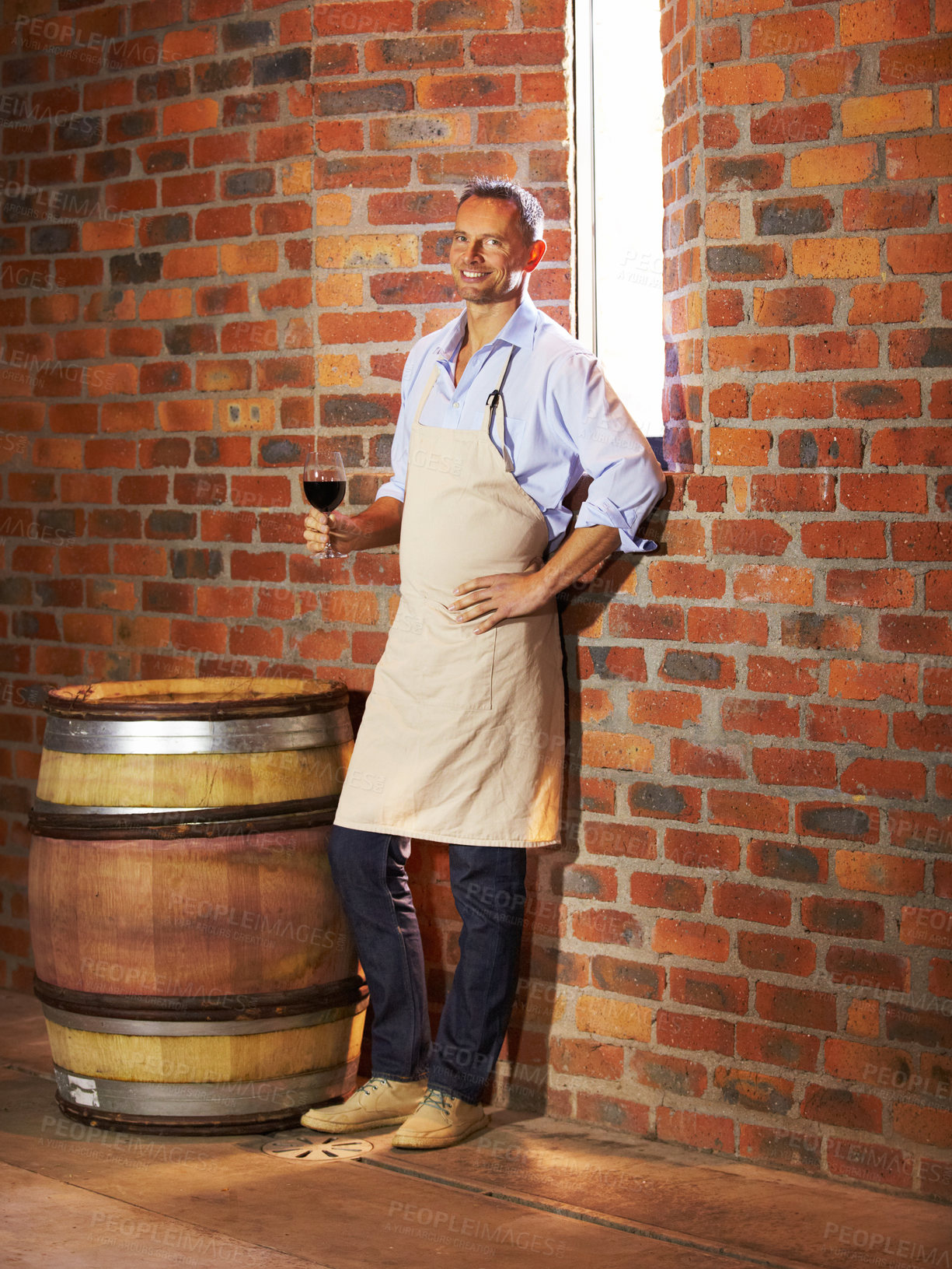 Buy stock photo Portrait, man sommelier with glass and taste in cellar or factory. Alcohol or drink, production storage or industry and happy mature male smile and standing by wooden barrel during wine tasting