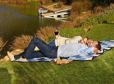 Buy stock photo Couple, picnic and lying by lake with wine outdoor, having fun and bonding on vacation. Portrait, alcohol and man and woman by river to relax, happiness and enjoying romantic time together in summer.