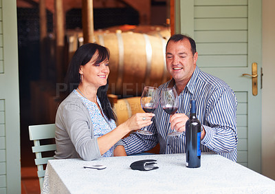 Buy stock photo A happy mature couple toasting with some red wine while sitting at a table on a wine cellar