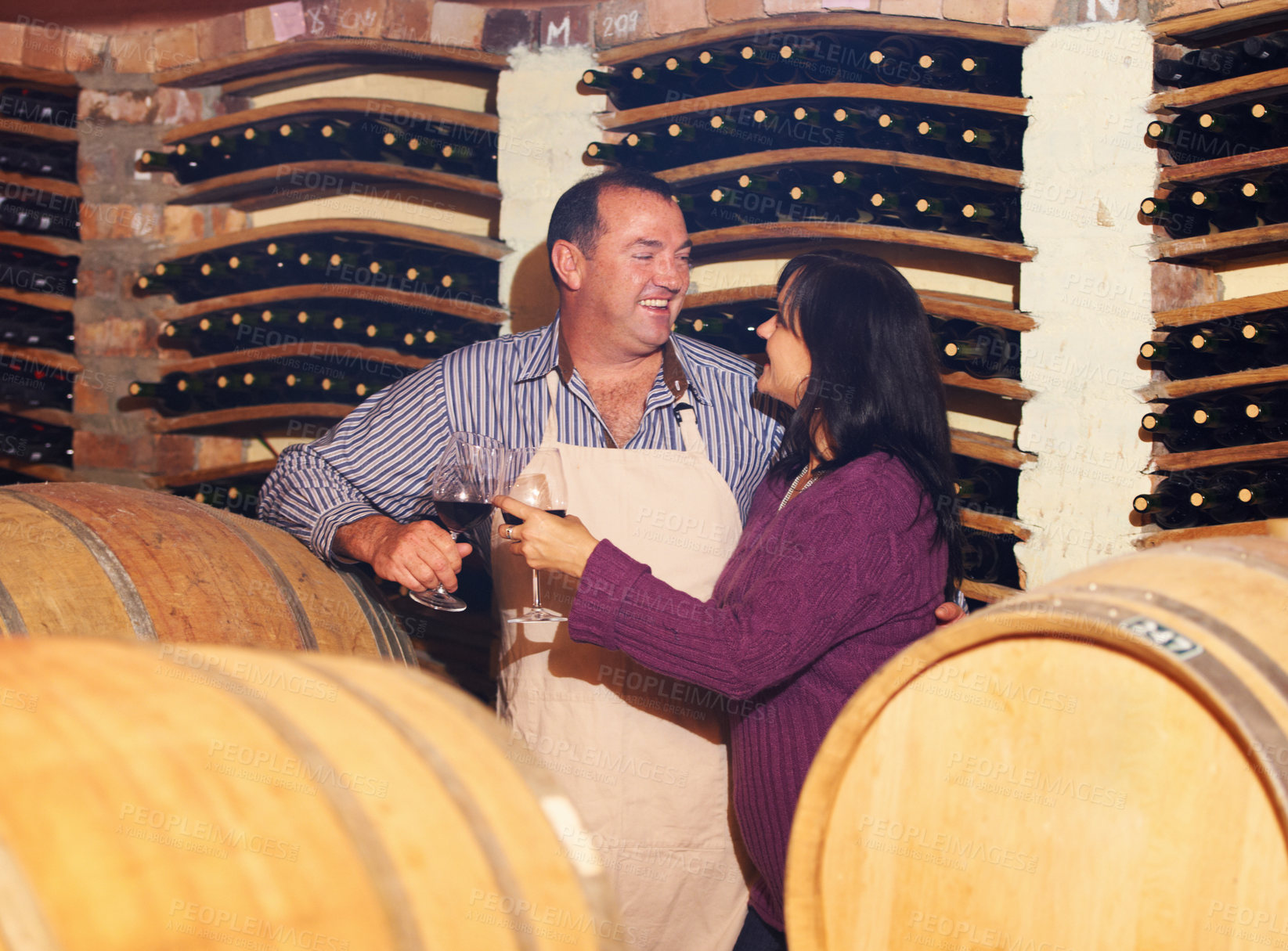Buy stock photo Wine, oak barrels and a couple in a cellar for the storage, production or fermentation of alcohol at a winery. Love, manufacturing or industry with a mature man and woman drinking a beverage together