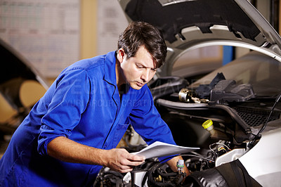 Buy stock photo A male mechanic reading some papers while working on the motor of a car