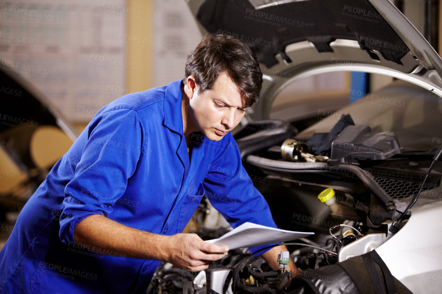 Buy stock photo A male mechanic reading some papers while working on the motor of a car