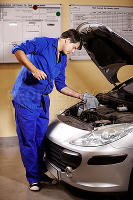 Buy stock photo A male mechanic wiping off the oil stick to measure a car's oil