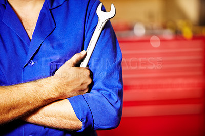 Buy stock photo Closeup male mechanic holding a spanner with his arms folded in a repair workshop. Tool in the hand of a man working on cars and performing services in a garage. For all your car care needs