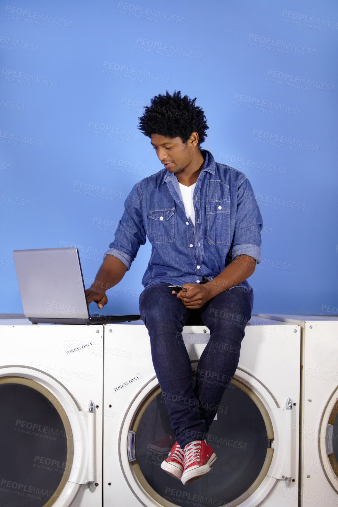 Buy stock photo Washing machine, laptop and phone of a black man for laundromat, communication and reading email. Cleaning, typing and a male employee or management of laundry room from the internet with tech