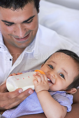 Buy stock photo A father feeding his baby boy a bottle of milk while sitting on the sofa