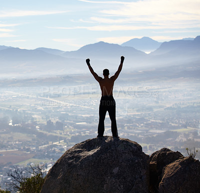 Buy stock photo Rearview of a man with his arms raised while standing on a mountain top