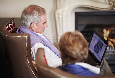 Buy stock photo Relax, senior couple with laptop in hotel lounge or restaurant checking social media on retirement vacation. Computer, old man and woman at fireplace in cozy holiday accommodation with online search.