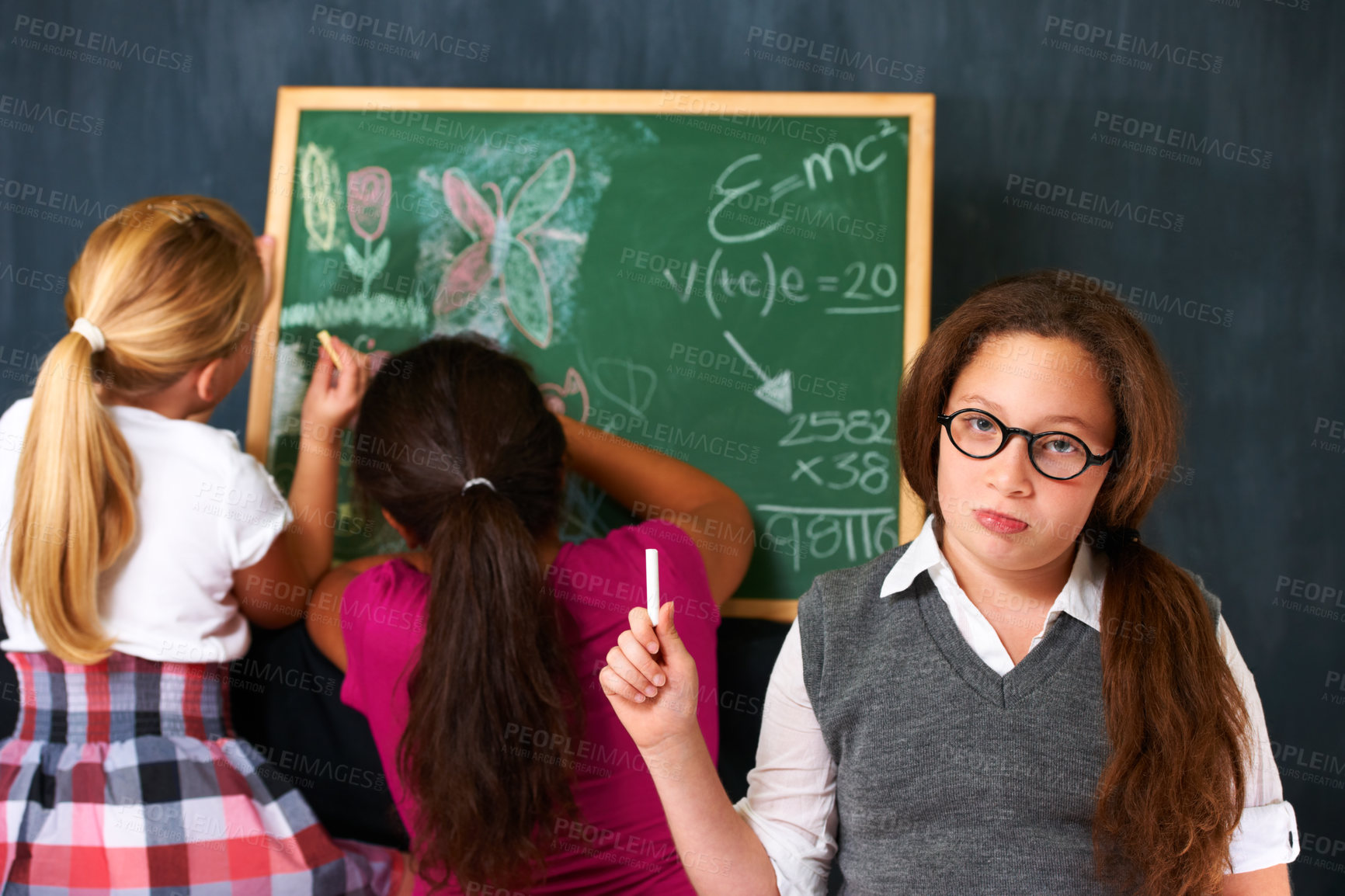 Buy stock photo Portrait of a cute brunette girl with two classmates playing on the chalkboard in class