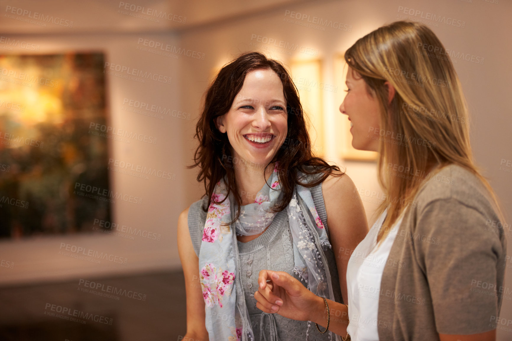 Buy stock photo Two young women share a laugh together while attending an art exhibition