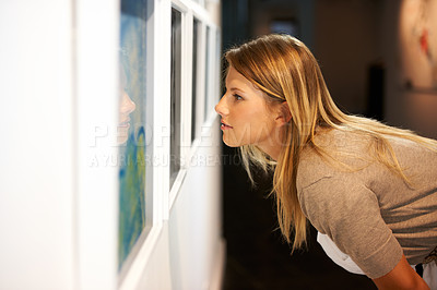 Buy stock photo Shot of a young woman looking at paintings in a gallery