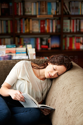 Buy stock photo Calm, library and woman reading a book on a sofa for literature while relaxing with shelves. Rest, happy and female person with a smile enjoying a fantasy story or novel on couch in bookstore or shop