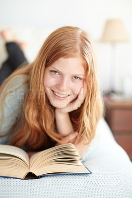 Buy stock photo Portrait of a young redhead reading her book and lying on her bed