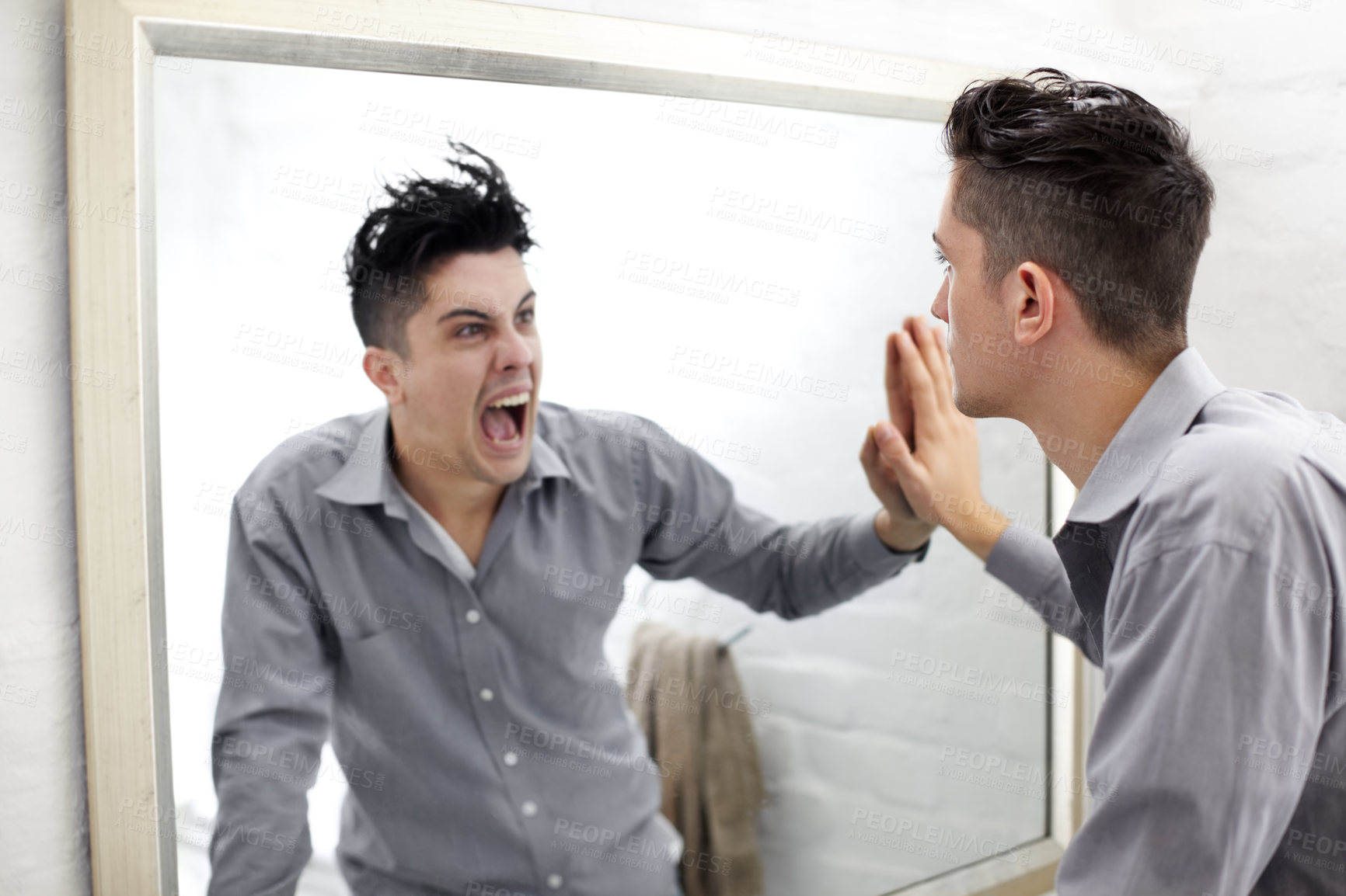 Buy stock photo Young man looking at a screaming reflection of himself in a mirror