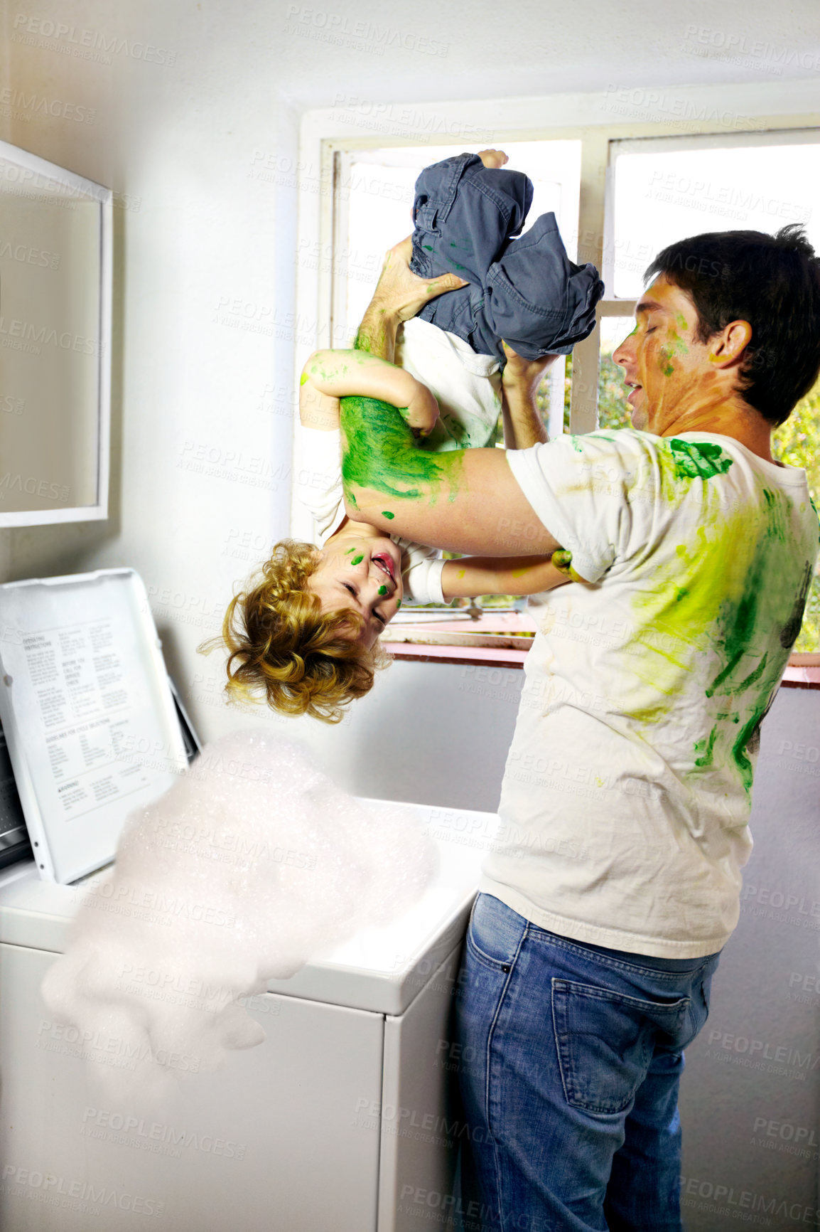 Buy stock photo Paint-covered father attempting to put his child in the washing machine