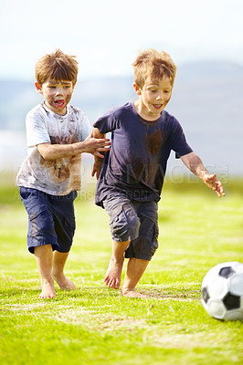 Buy stock photo Two cute little boys playing soccer together outside while covered in mud