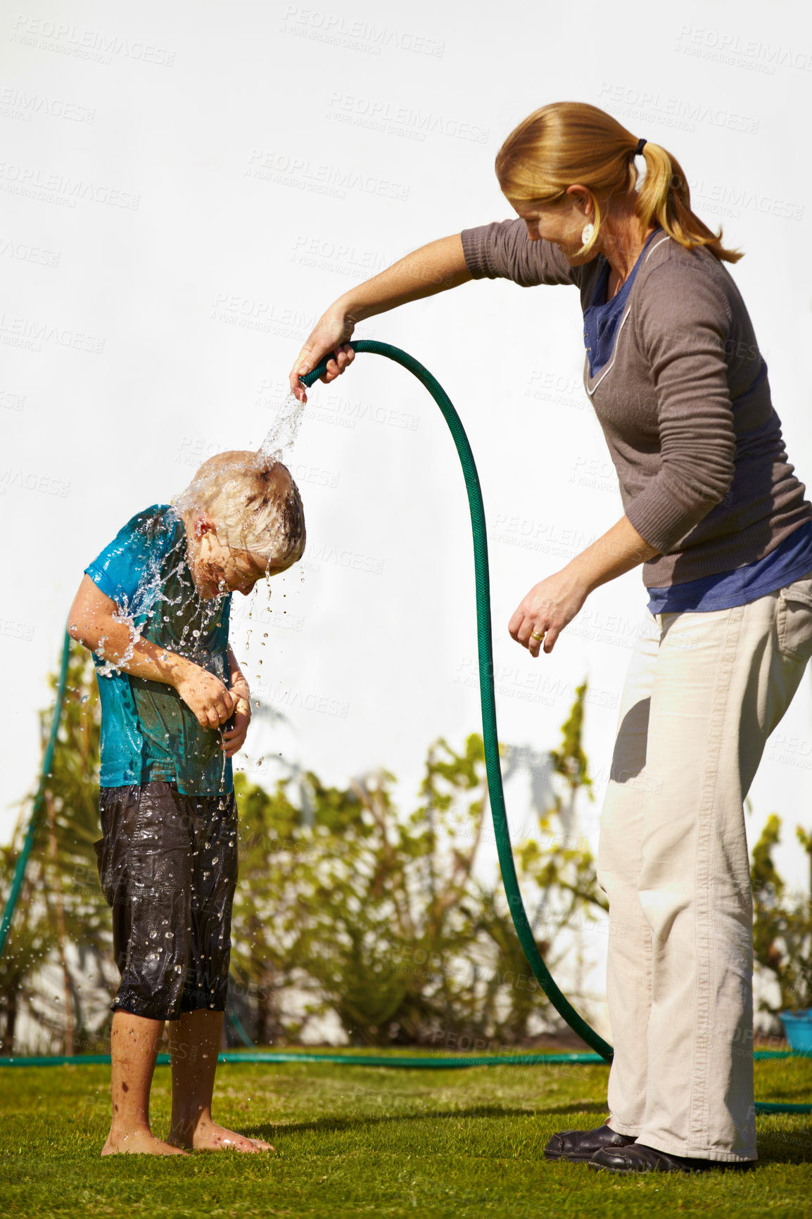 Buy stock photo Boy, woman and hose pipe with water fun, splash and playing outdoor in backyard or garden for sunshine. Kid, people or mother on grass or lawn with happiness, activity and enjoyment in summer weather