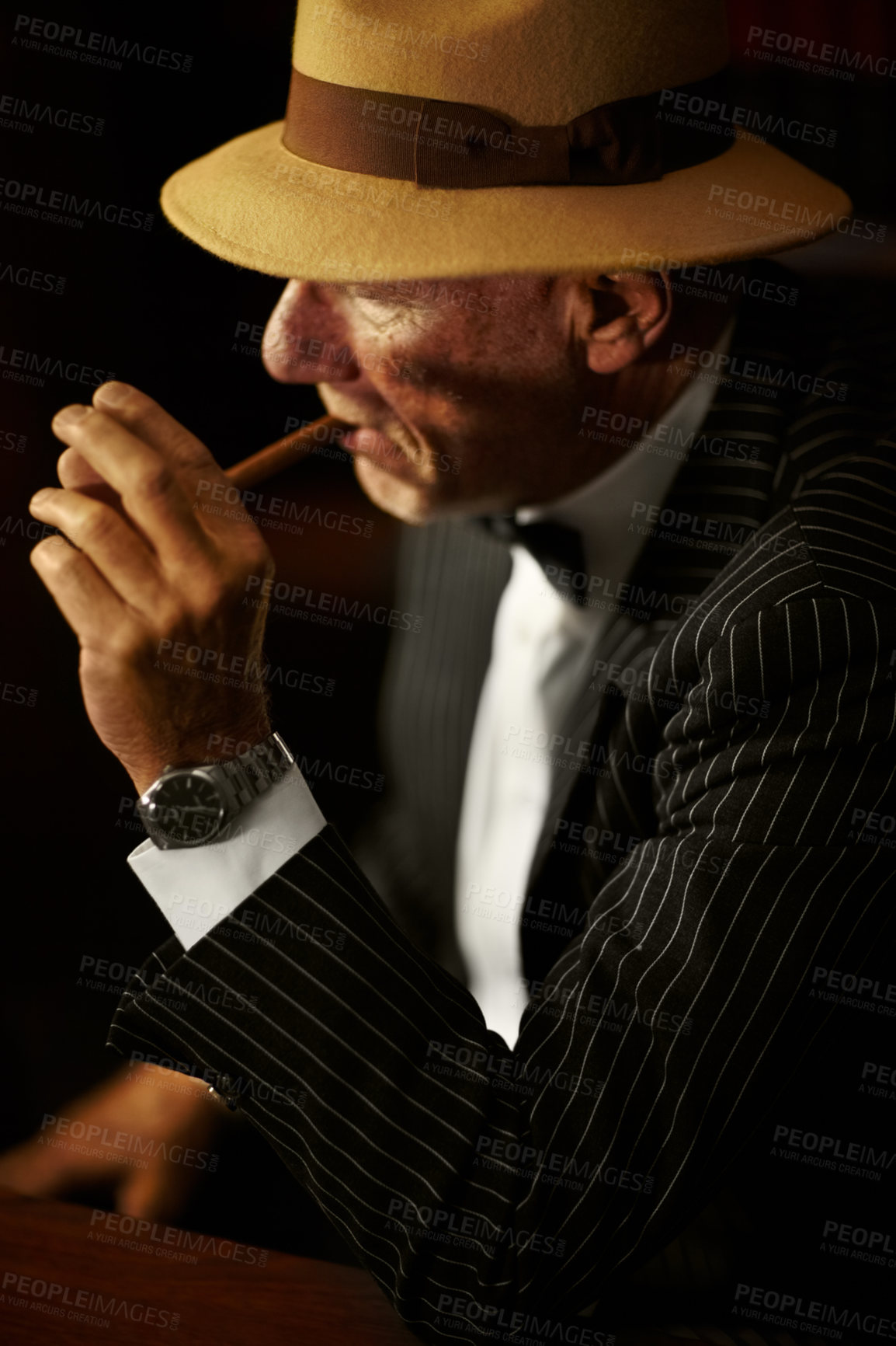 Buy stock photo Senior mob boss isolated against black background in studio. Mafia leader wearing a hat and looking serious while smoking tobacco in a pipe. Elderly gangster looking contemplative and smoking a cigar