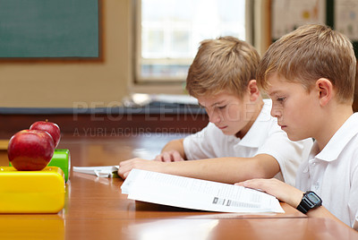 Buy stock photo Two young schoolboys sitting in class and reading their work