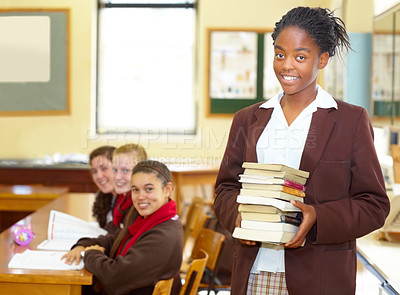 Buy stock photo Smiling young high school student holding books while standing in the classroom