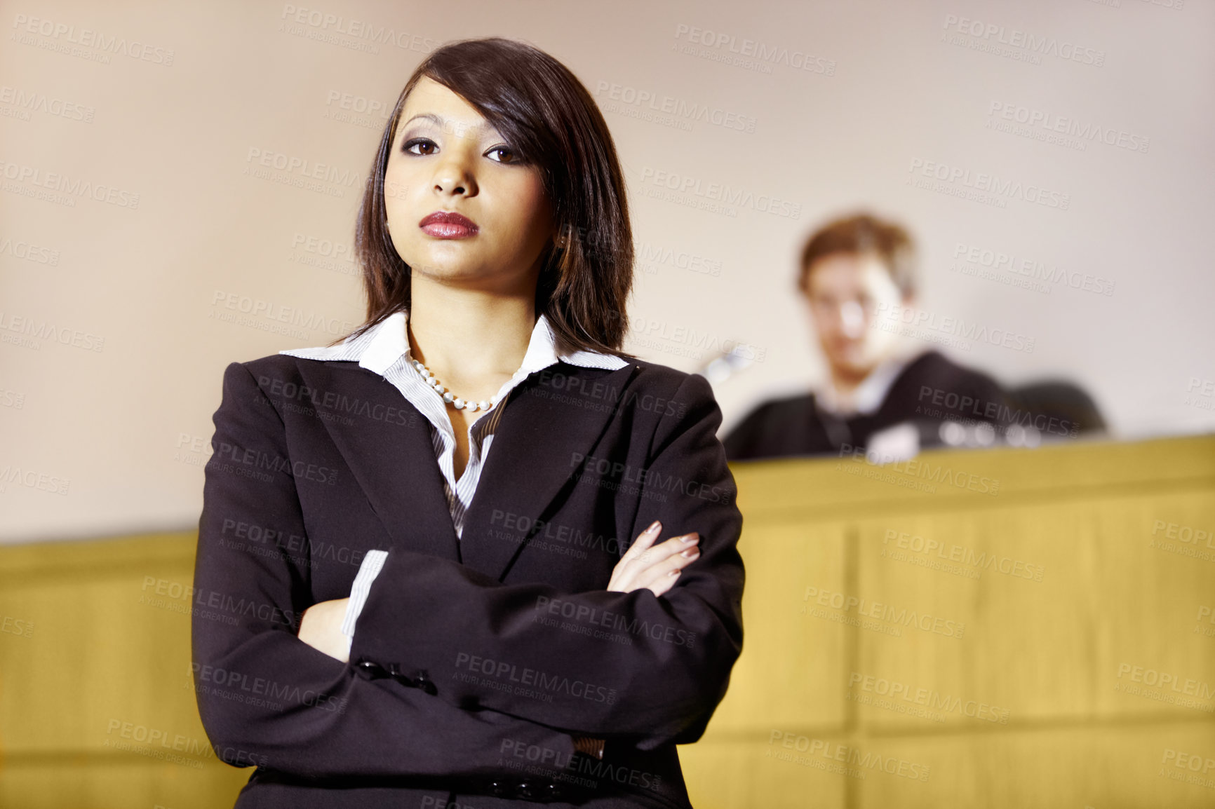 Buy stock photo Stern young advocate standing in the courtroom with her arms folded. Lawyer or defense attorney posing with her hand folded in courtroom. A lady in courtroom.
