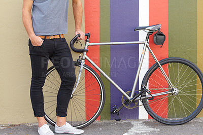 Buy stock photo Cropped shot of a stylishly dressed young man standing next to a bicycle against a colourful background