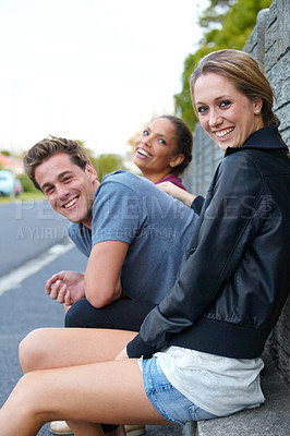 Buy stock photo Portrait of three young friends sitting on a roadside bench