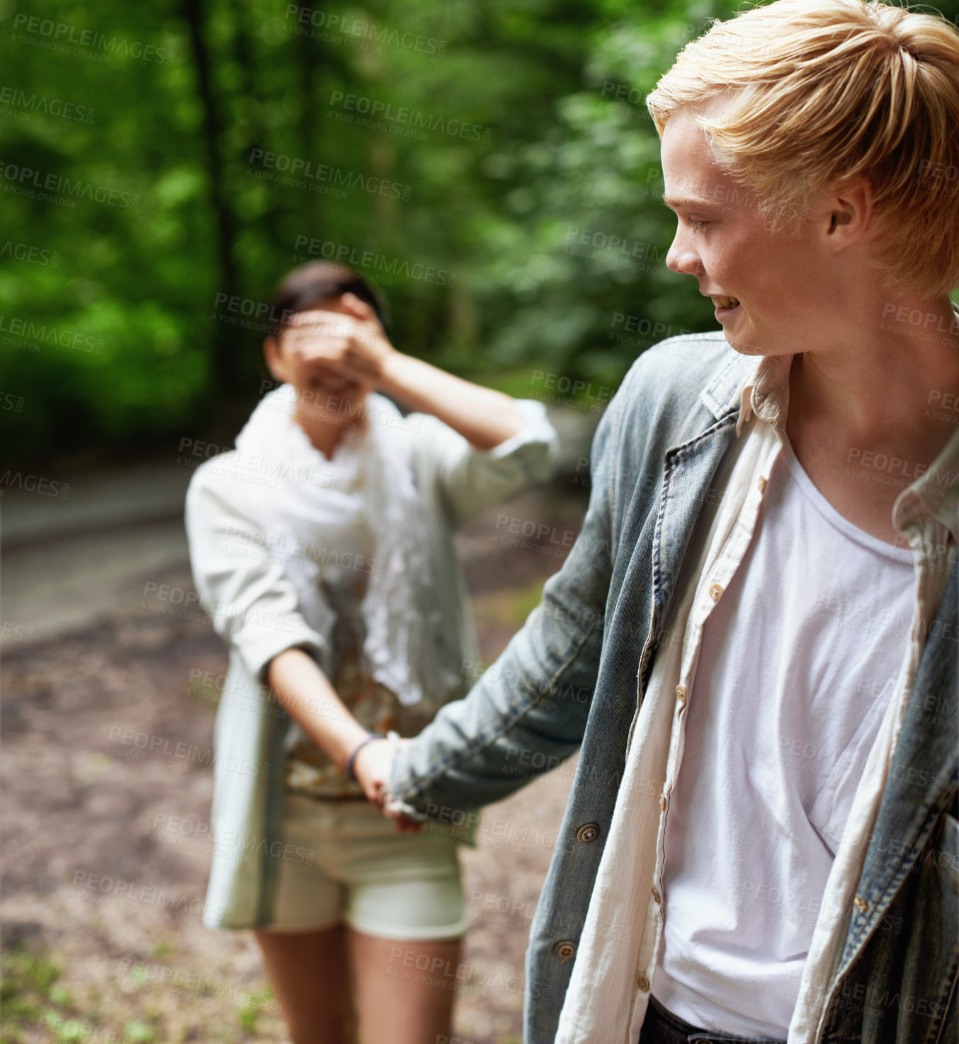 Buy stock photo A girl covering her eyes with her hand is led through the forest by her boyfriend