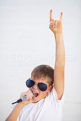 Buy stock photo Young boy lost in song while holding a microphone and wearing sunglasses