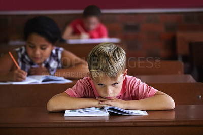 Buy stock photo A young boy resting his head on his arms as he sits in a classroom looking bored