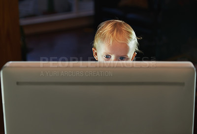 Buy stock photo Curious kid browsing using a desktop pc alone and unsupervised, looking at some age restricted content on the online internet at night. Little baby boy sitting behind the screen of a computer at home