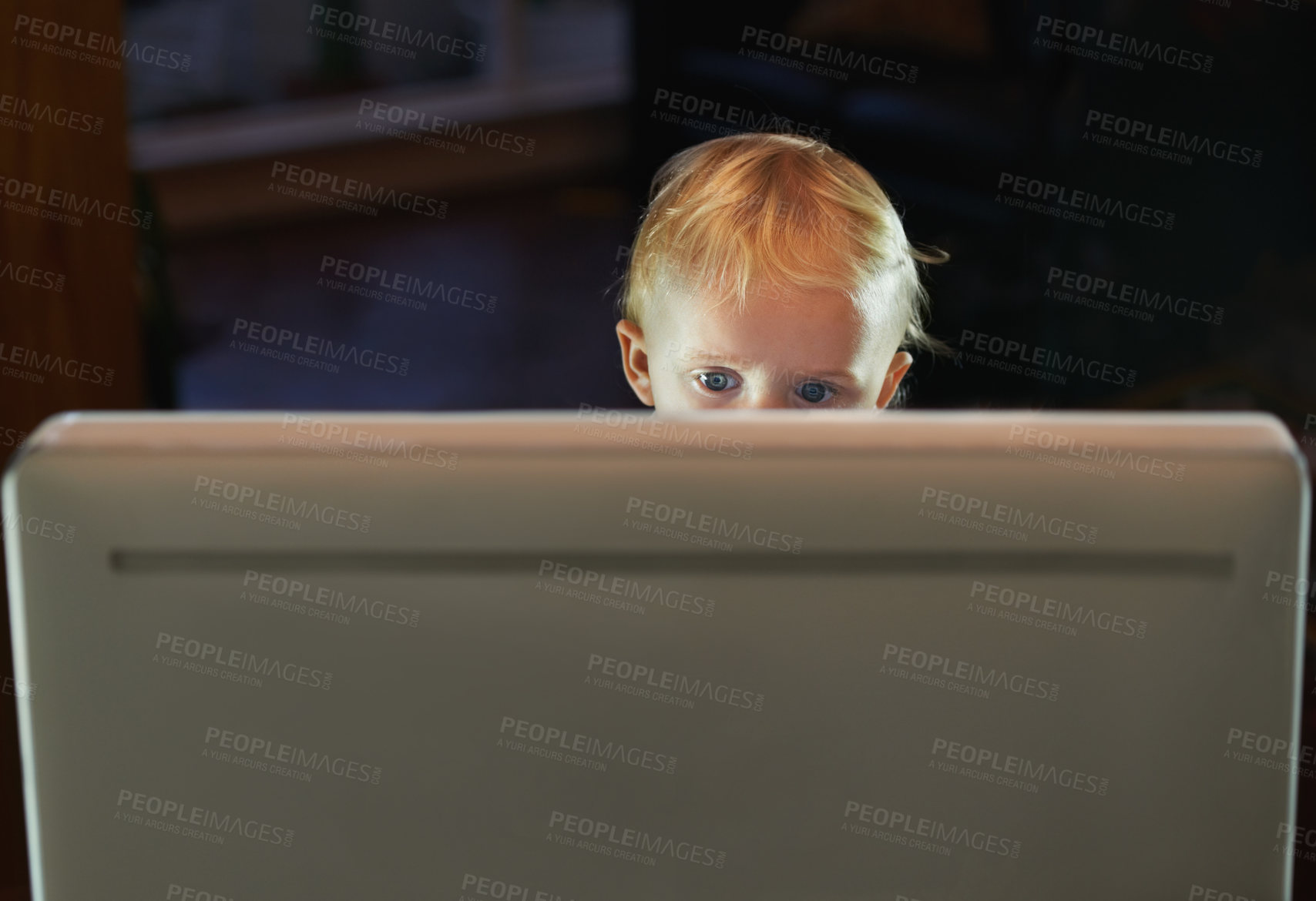 Buy stock photo Curious kid browsing using a desktop pc alone and unsupervised, looking at some age restricted content on the online internet at night. Little baby boy sitting behind the screen of a computer at home