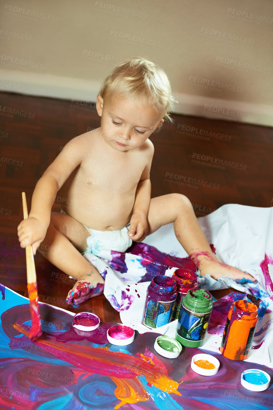 Buy stock photo Creative little baby boy painting with vibrant colors and paints. Small child sitting alone in a diaper and enjoying creative activity at home. Practicing motor skills in fun, artistic activities