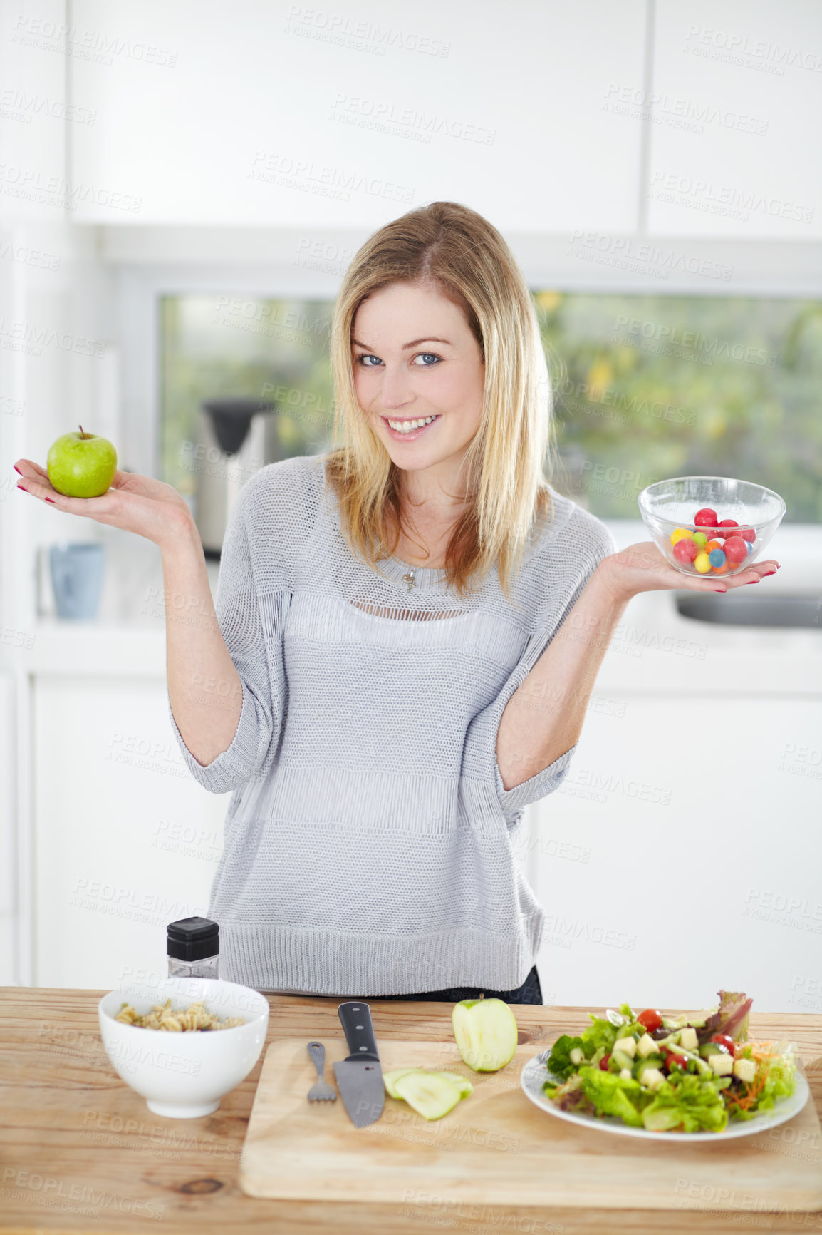 Buy stock photo Choice, sweets and woman decide on healthy food in a kitchen for a diet and holding an apple and candy in home. Portrait, smile an happy female person with fruit for nutrition as lunch meal
