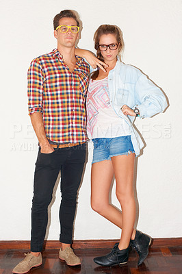 Buy stock photo A young hipster couple standing against a white wall while wearing glasses