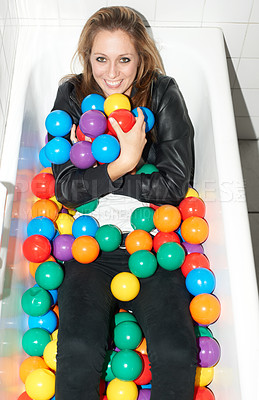 Buy stock photo Portrait, balls and happy woman in bathtub for fashion, style and trendy hipster at home. Smile of person in tub with color, sphere and plastic with body in bathroom, relax in edgy and cool clothes