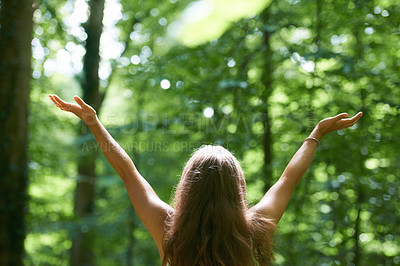 Buy stock photo Rearview of a beautiful young woman with her arms raised while standing in a forest