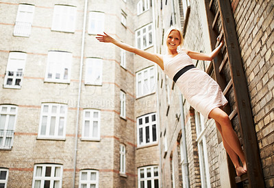 Buy stock photo A gorgeous young woman posing on the ladder of a fire escape