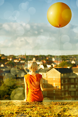 Buy stock photo Rear view of a young woman sitting with a balloon and a city in the background