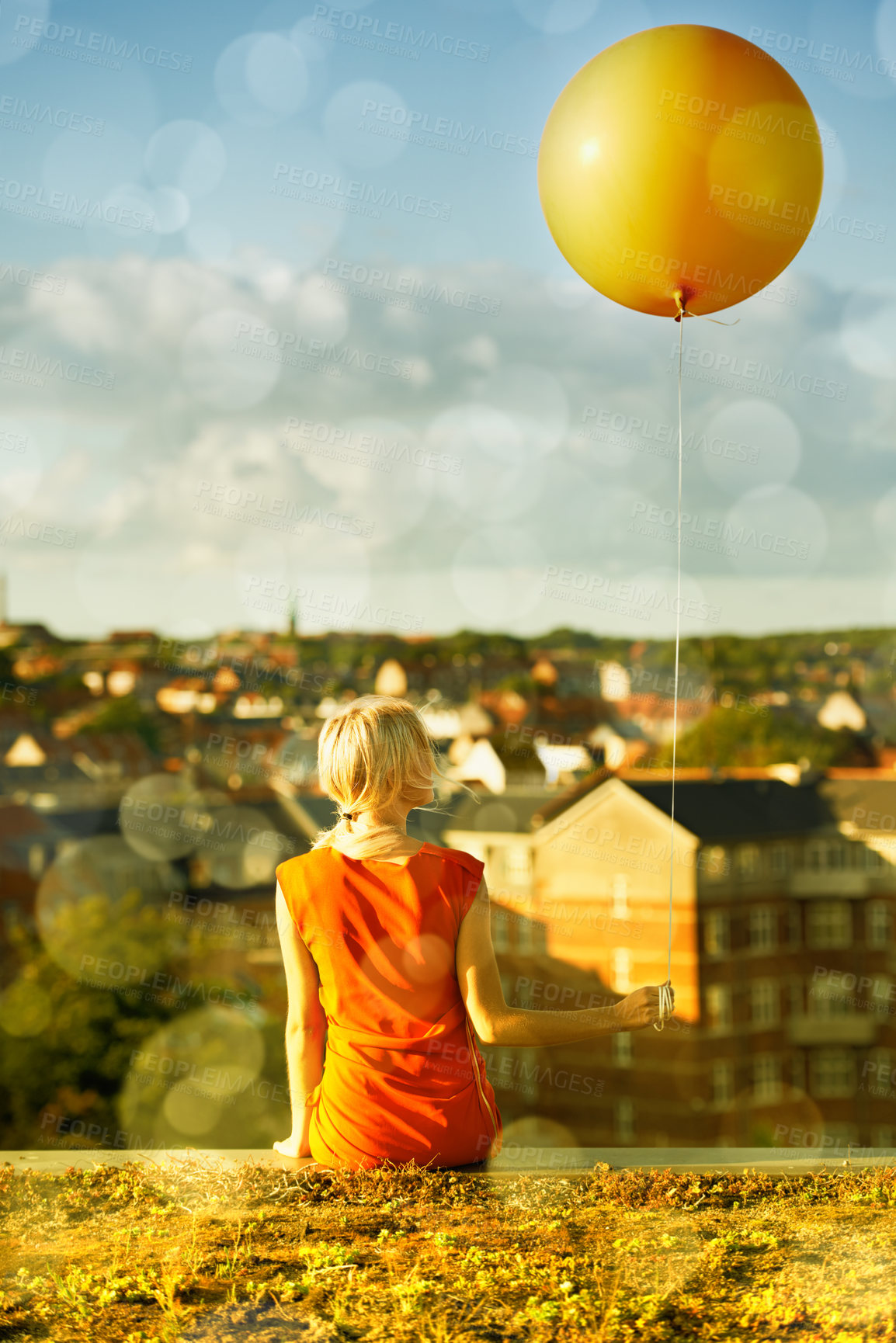 Buy stock photo Rear view of a young woman sitting with a balloon and a city in the background