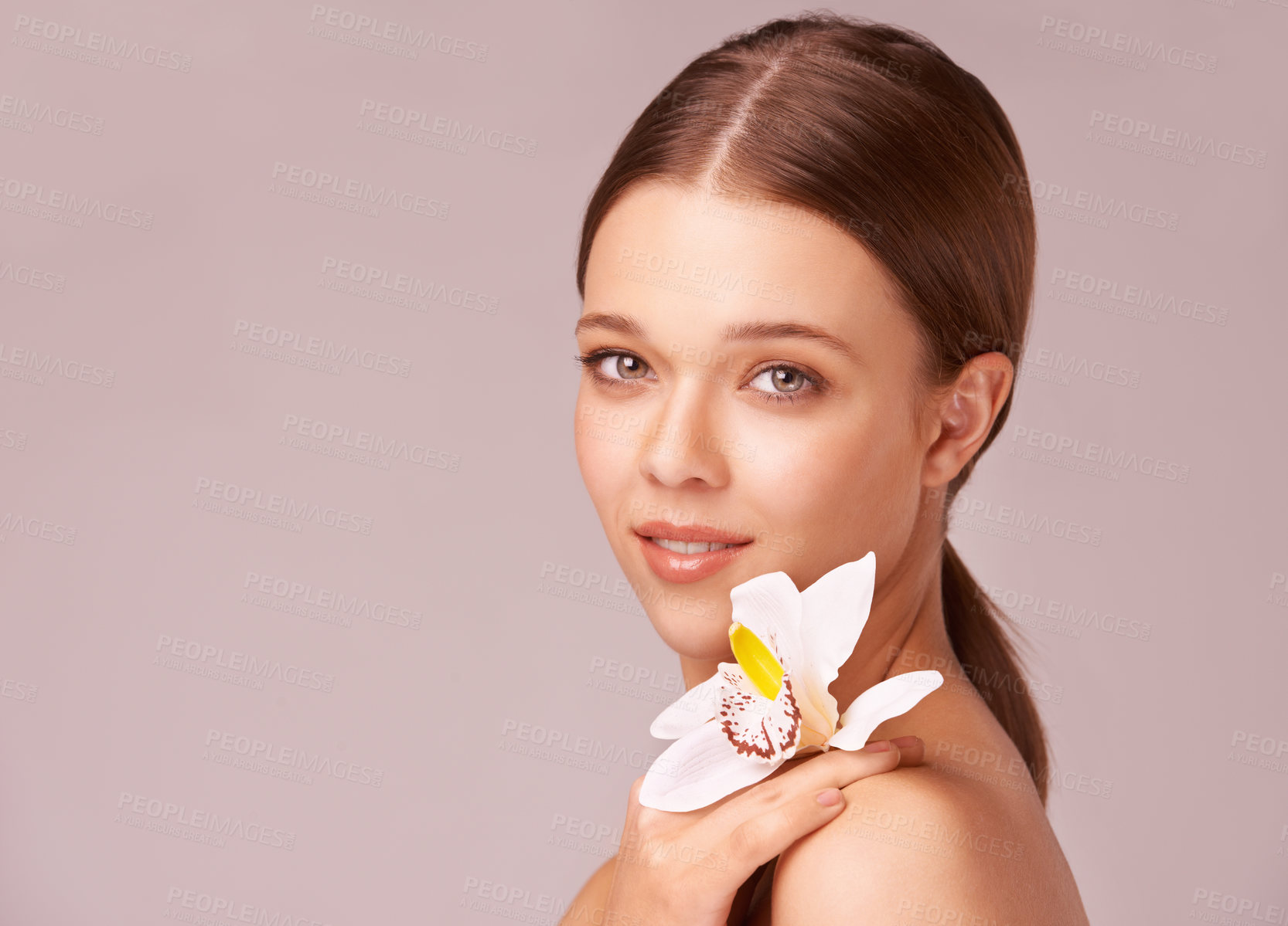 Buy stock photo Beautiful young woman holding an orchid at her shoulder against a pink background